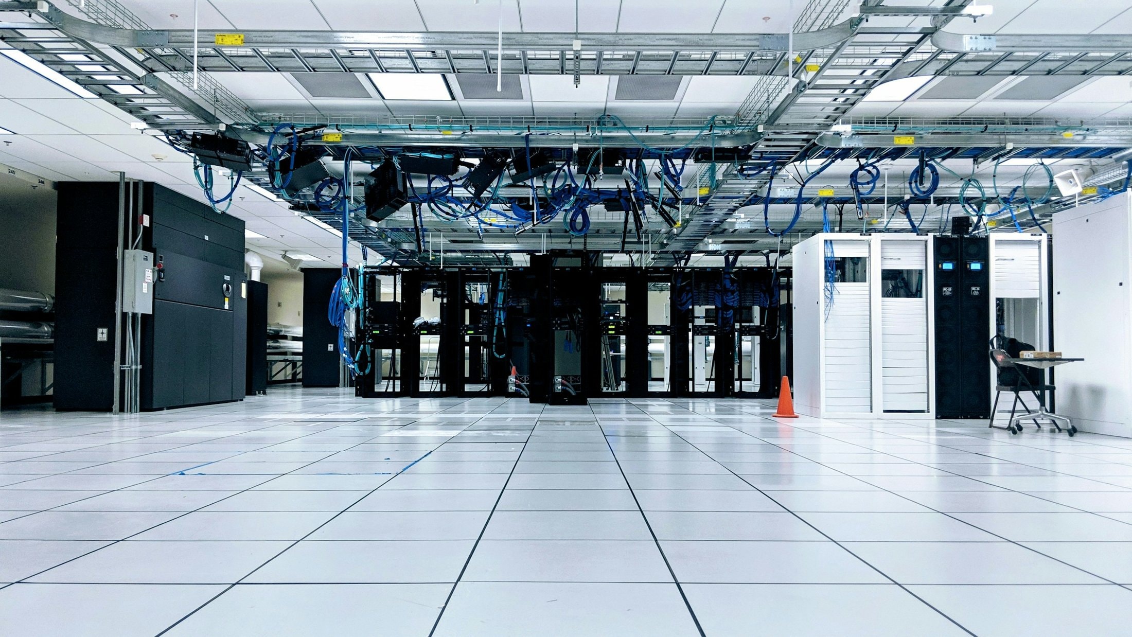 Data hall with a raised white floor, rows of server cabinets and overhead cable trays