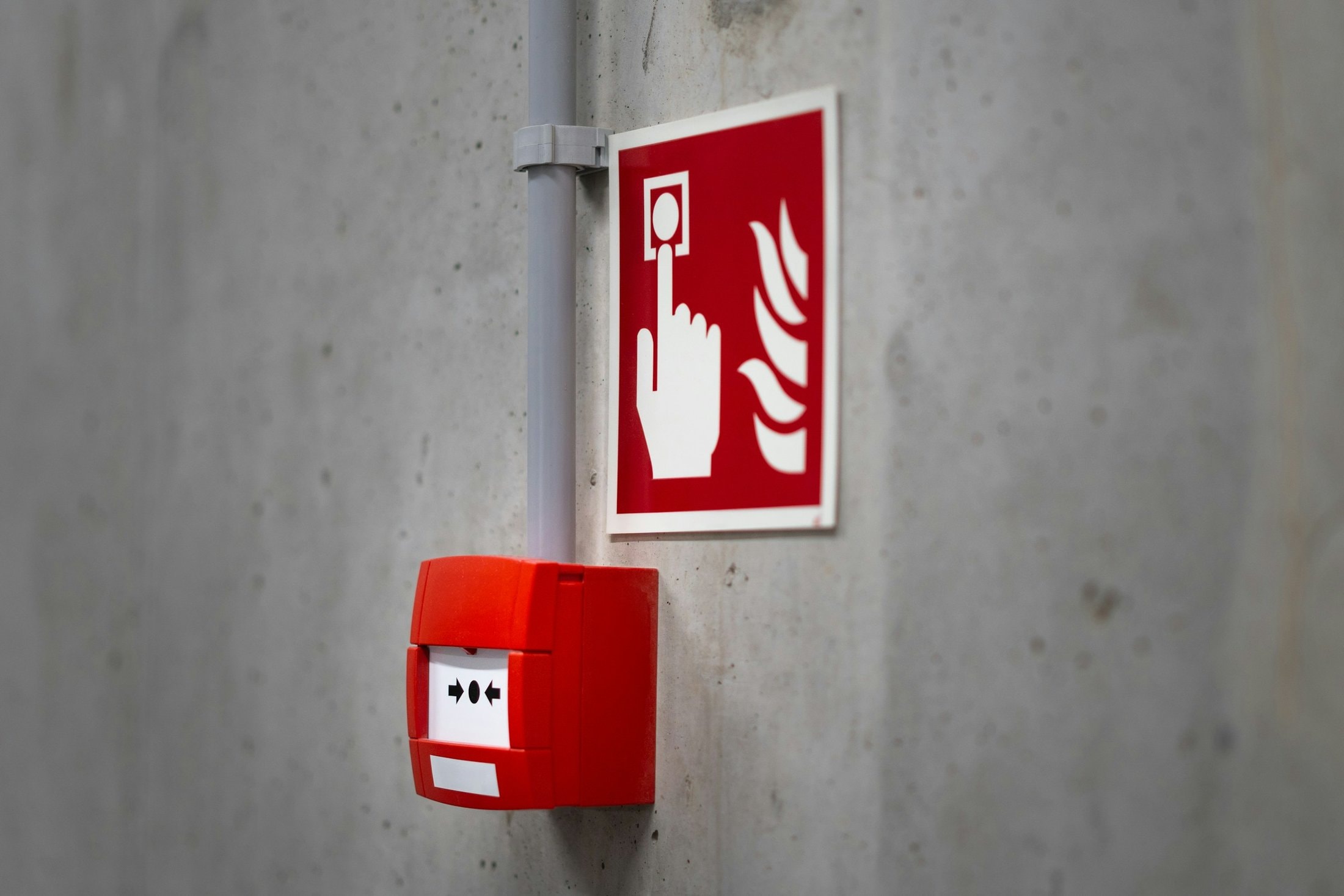 Red manual fire alarm call point and sign on a concrete wall