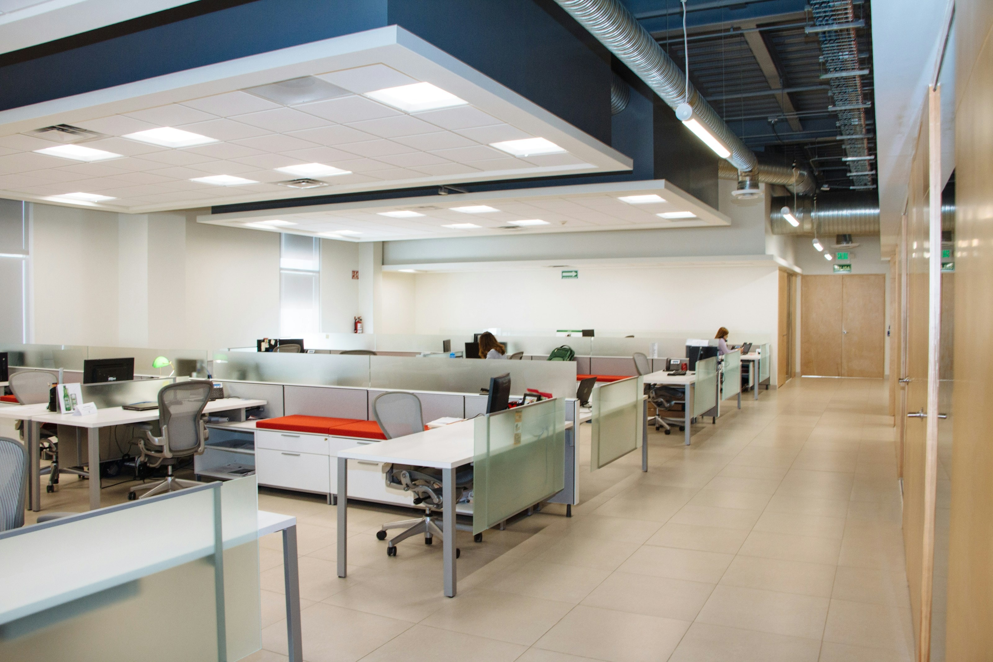 Open-plan office with rows of white desks, frosted glass screens and an exposed services ceiling