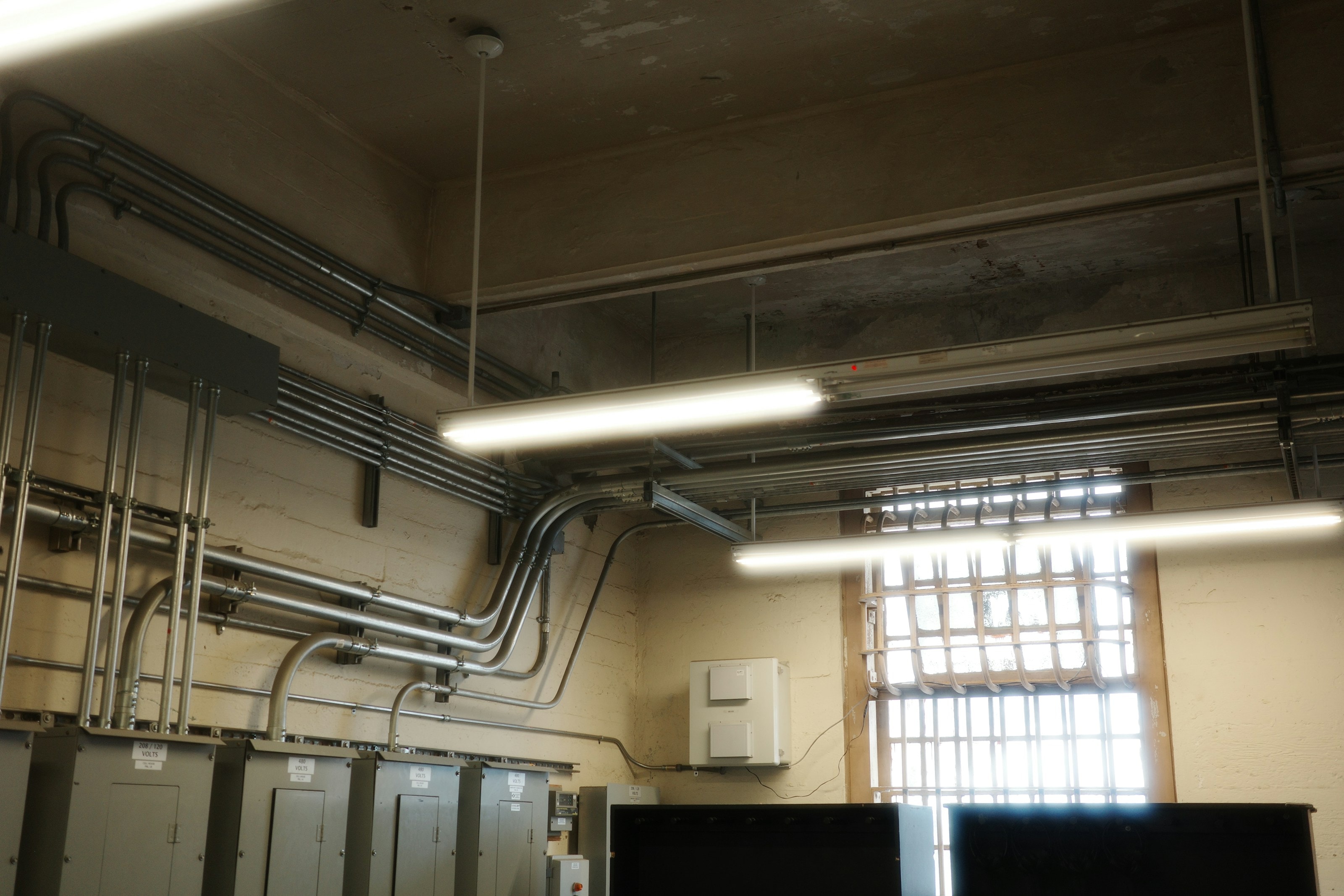 Electrical conduit runs, distribution boards and new light fittings across a bare plant-room ceiling